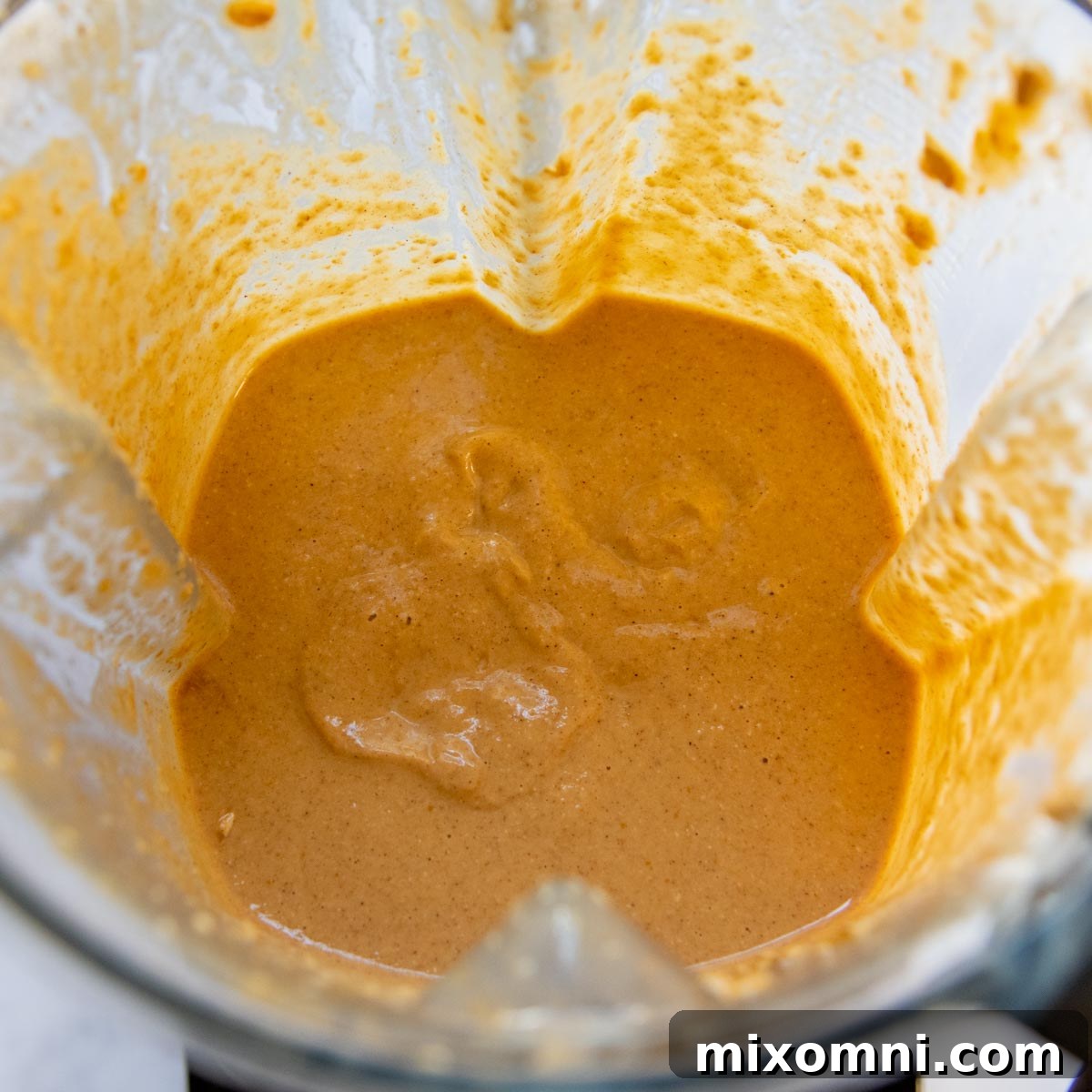 Smooth, thick pumpkin pancake batter swirling in a blender after being processed, showcasing its creamy consistency before resting.