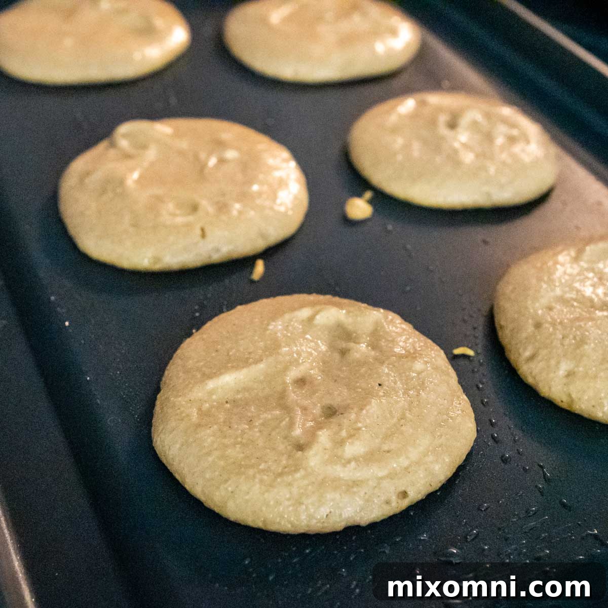 Golden pumpkin pancake batter cooking on a hot griddle, showing the perfect sizzle and early stages of cooking.