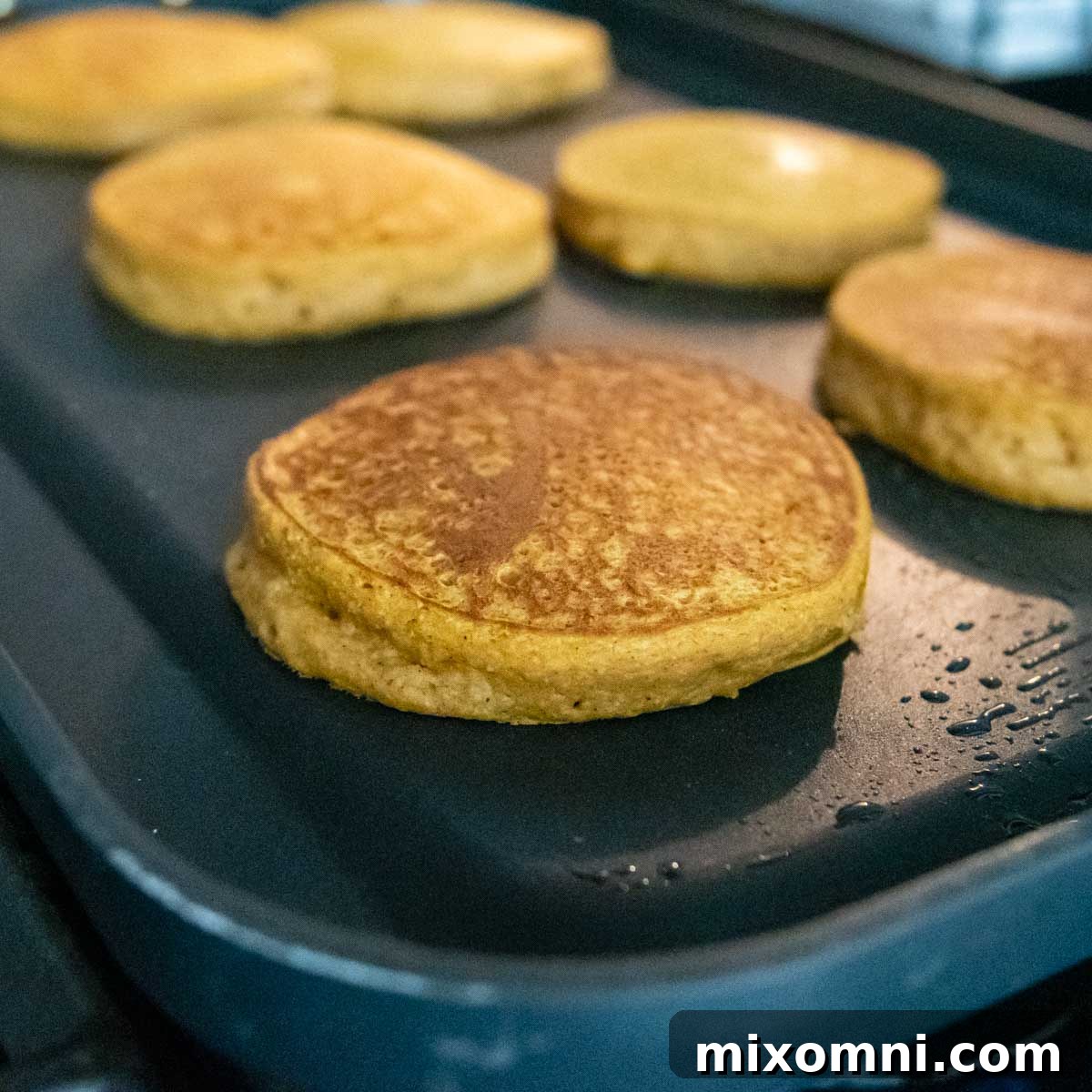 A batch of perfectly cooked pumpkin oatmeal pancakes sizzling on a griddle, showcasing their golden-brown exterior and fluffy appearance.