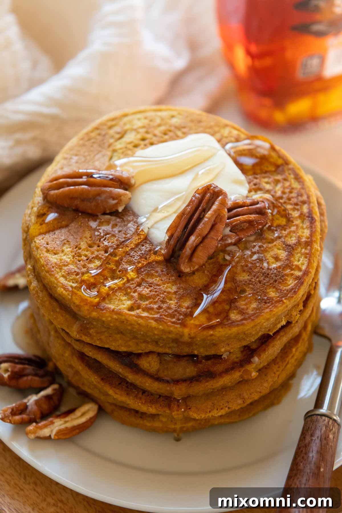 An overhead view of a tall stack of warm pumpkin oatmeal pancakes, generously drizzled with rich maple syrup, ready to be enjoyed as a delightful breakfast.
