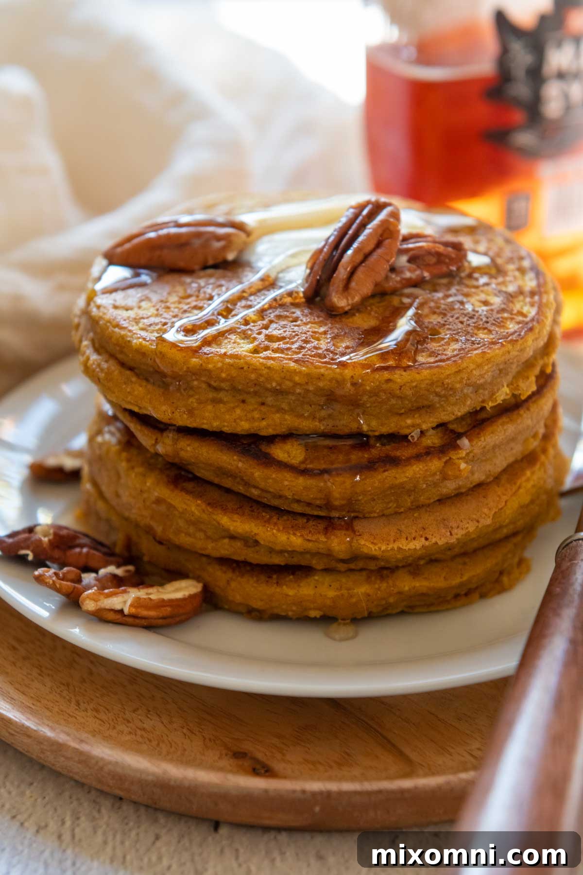 A delectable stack of pumpkin oatmeal pancakes, generously topped with a dollop of butter and a scattering of crunchy pecans, glistening with maple syrup.