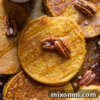 An overhead shot of a stack of fluffy pumpkin oatmeal pancakes, beautifully presented with a rich drizzle of syrup and a sprinkle of nuts, ready to serve.