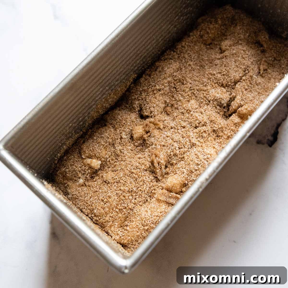 The first half of the bread dough is spread in a loaf pan, and the dry cinnamon sugar mixture is sprinkled evenly over it.