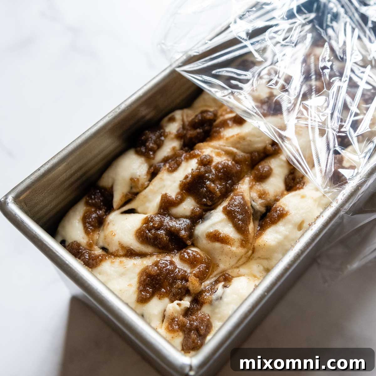 The bread dough has risen significantly in the loaf pan, showing a pronounced swirl pattern before it goes into the oven.