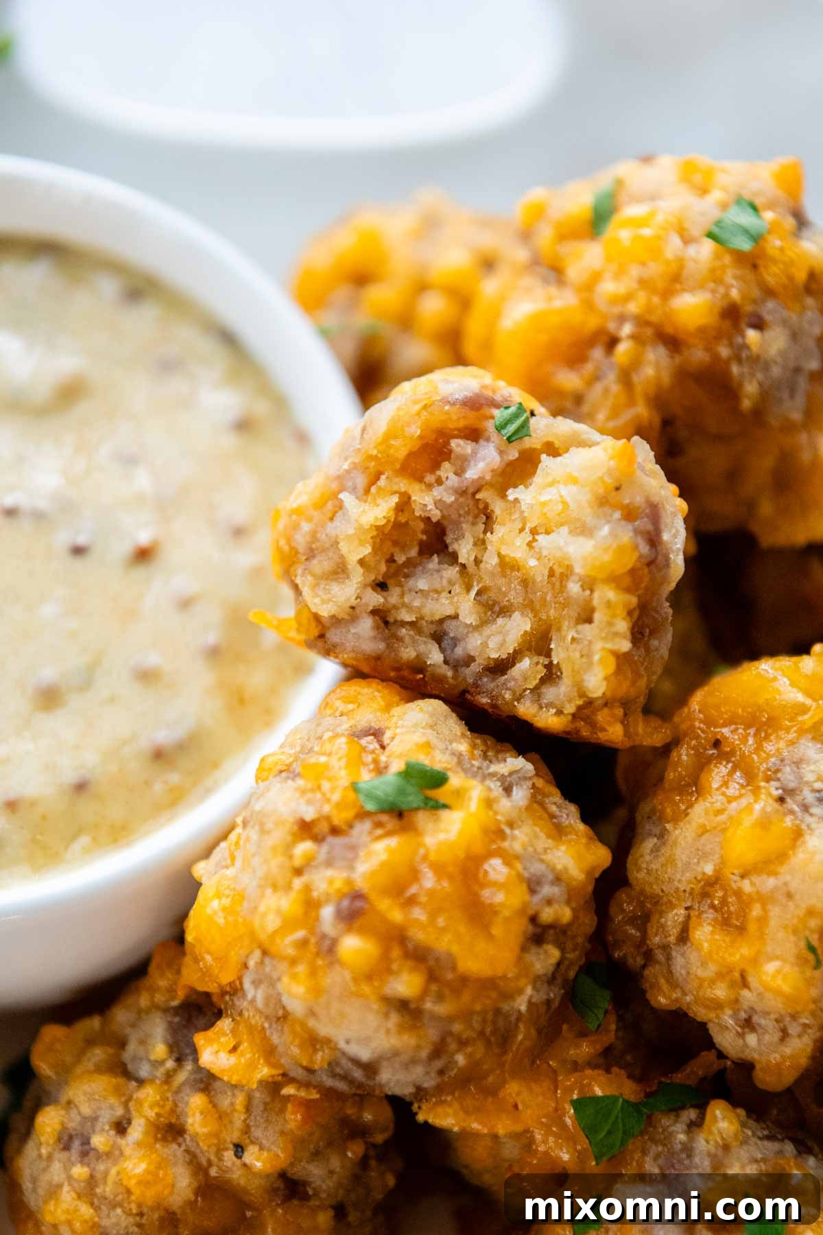 a bite taken out of one of the balls with dipping sauce in the background.