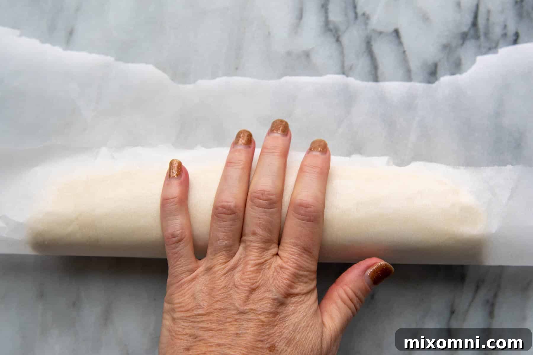 A baker's hands expertly rolling gluten-free shortbread dough into a log using parchment paper for an even shape.