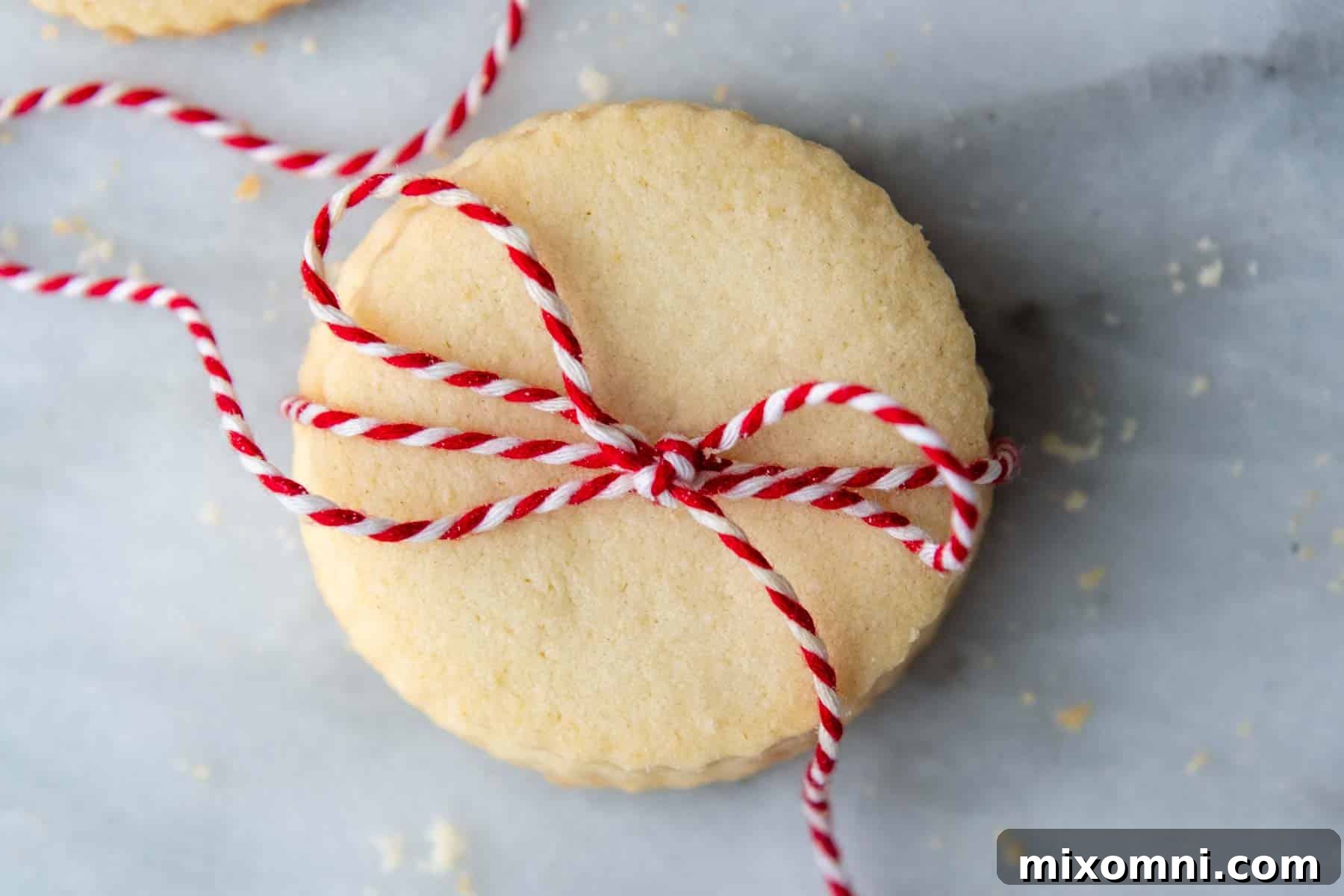 An overhead shot of several beautifully arranged gluten-free shortbread cookies, some with a festive red string wrapped around them, presented on a rustic surface.