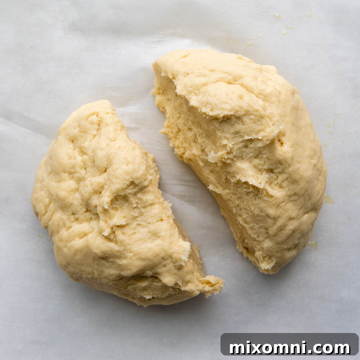 Gluten-free baguette dough meticulously divided into two equal halves on parchment paper, ready for shaping.