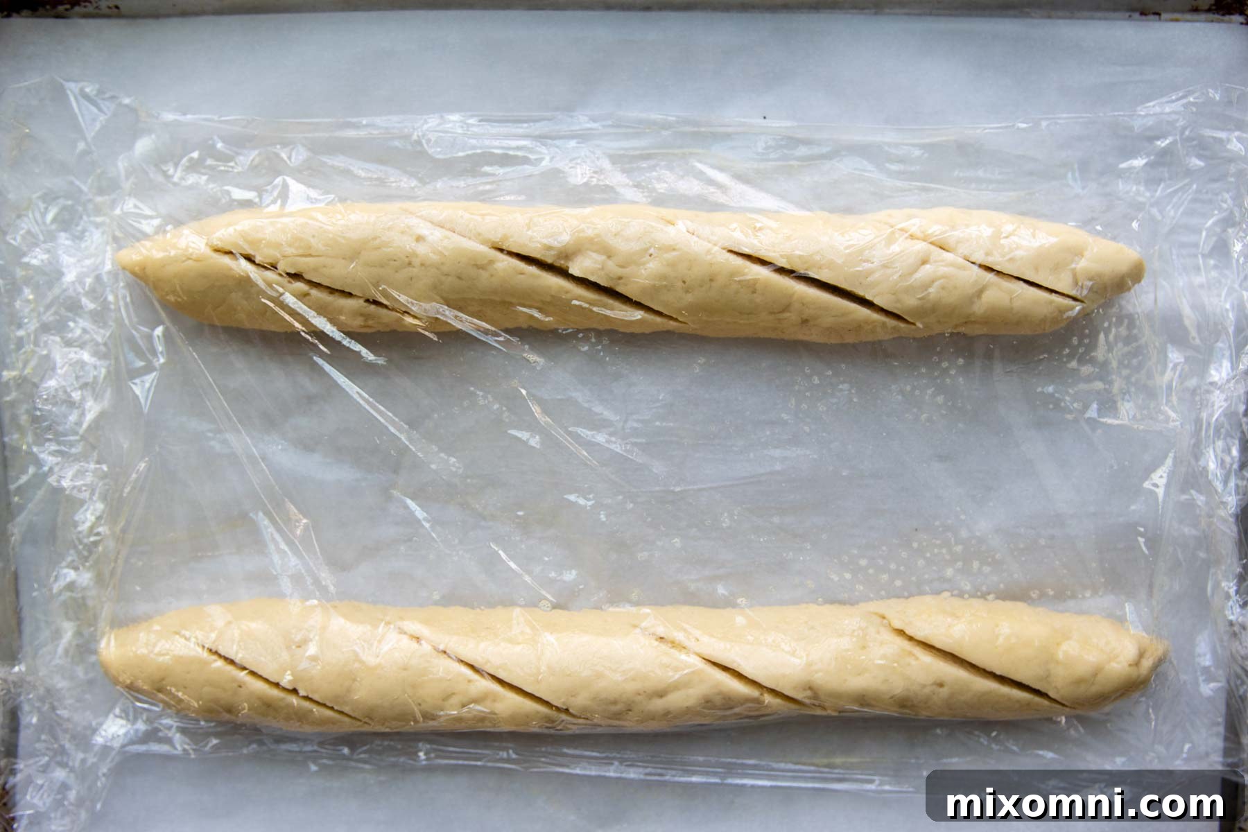 Two perfectly shaped gluten-free baguette logs resting on parchment paper before their crucial rising stage.