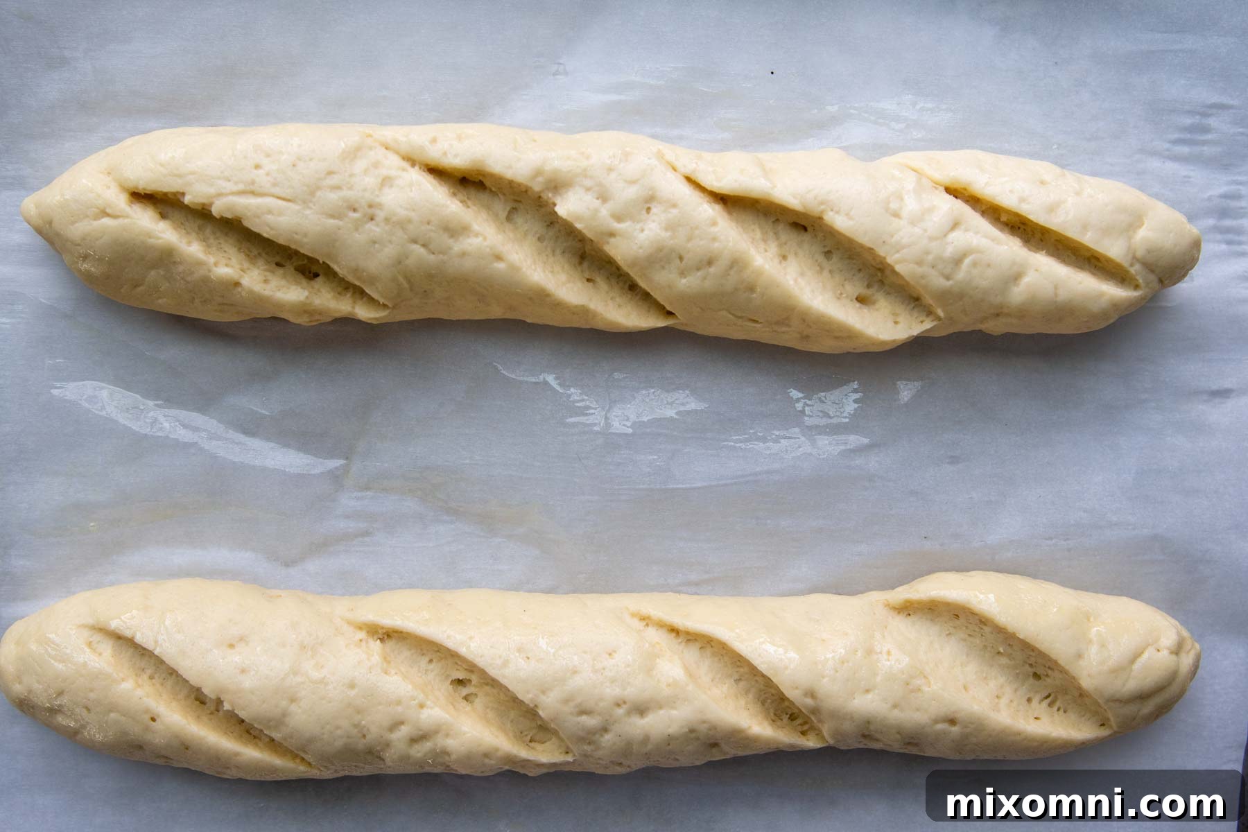 Gluten-free baguettes visibly risen on a baking sheet, showcasing their readiness for the oven.