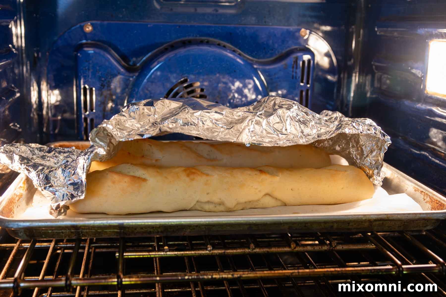 Gluten-free French bread baking in the oven, with aluminum foil loosely tented over the loaves to prevent excessive browning.