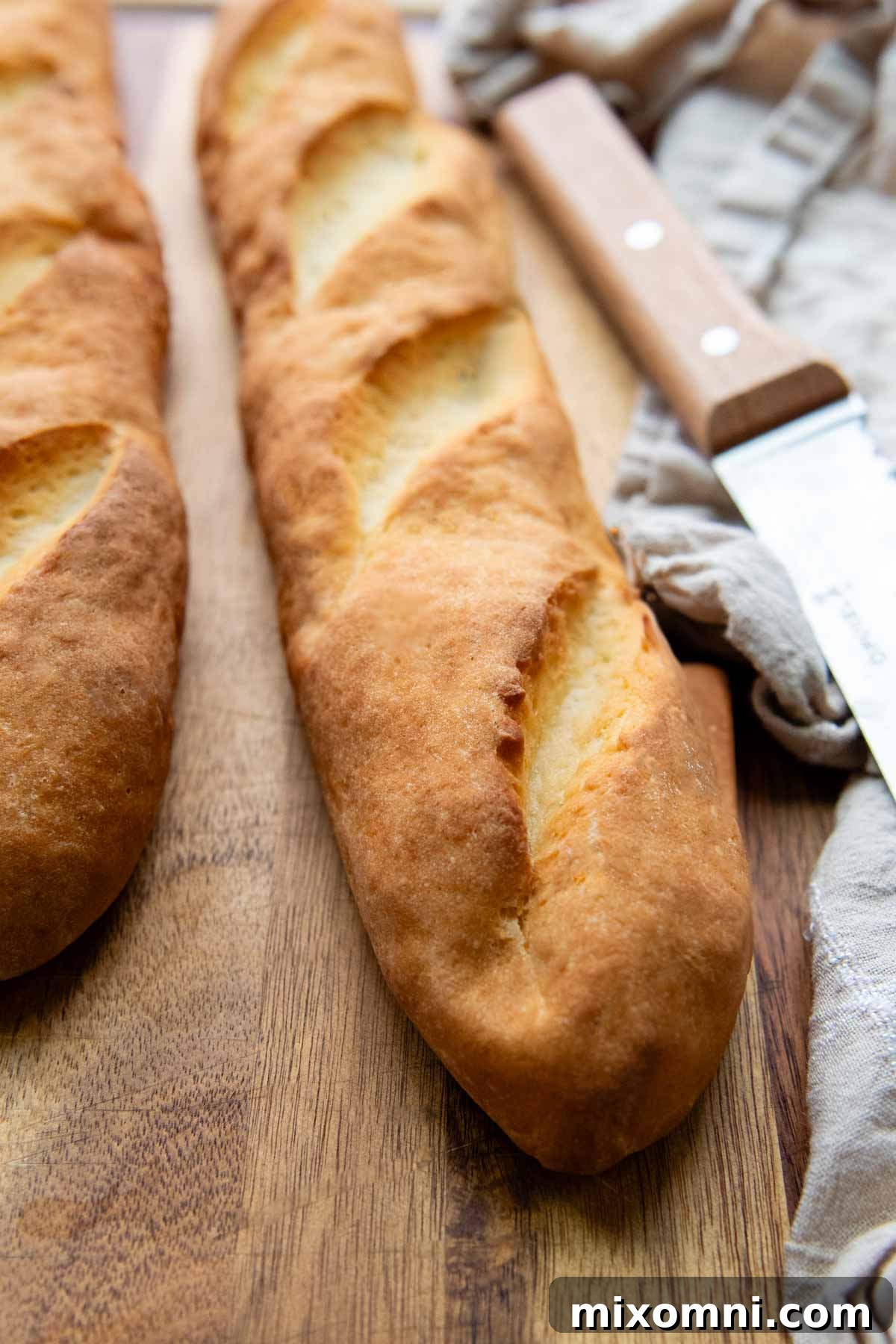 Two freshly baked gluten-free French bread loaves cooling on a wooden cutting board, showcasing their golden-brown crusts and perfect shape.