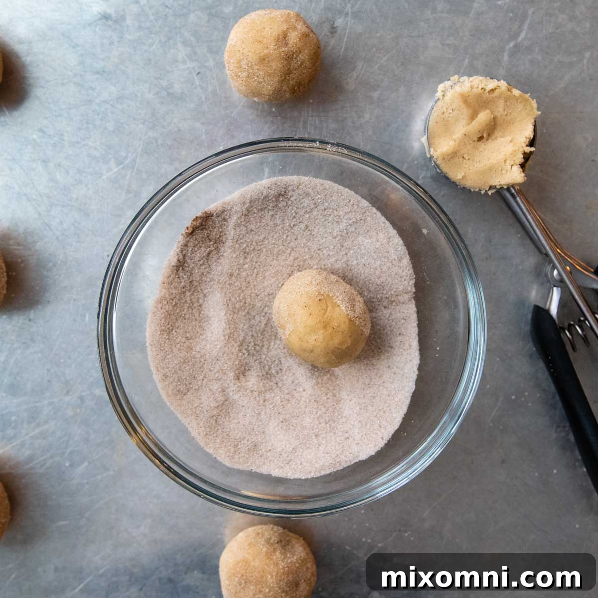 Gluten-free cookie dough balls generously rolled in cinnamon sugar, ready for baking.