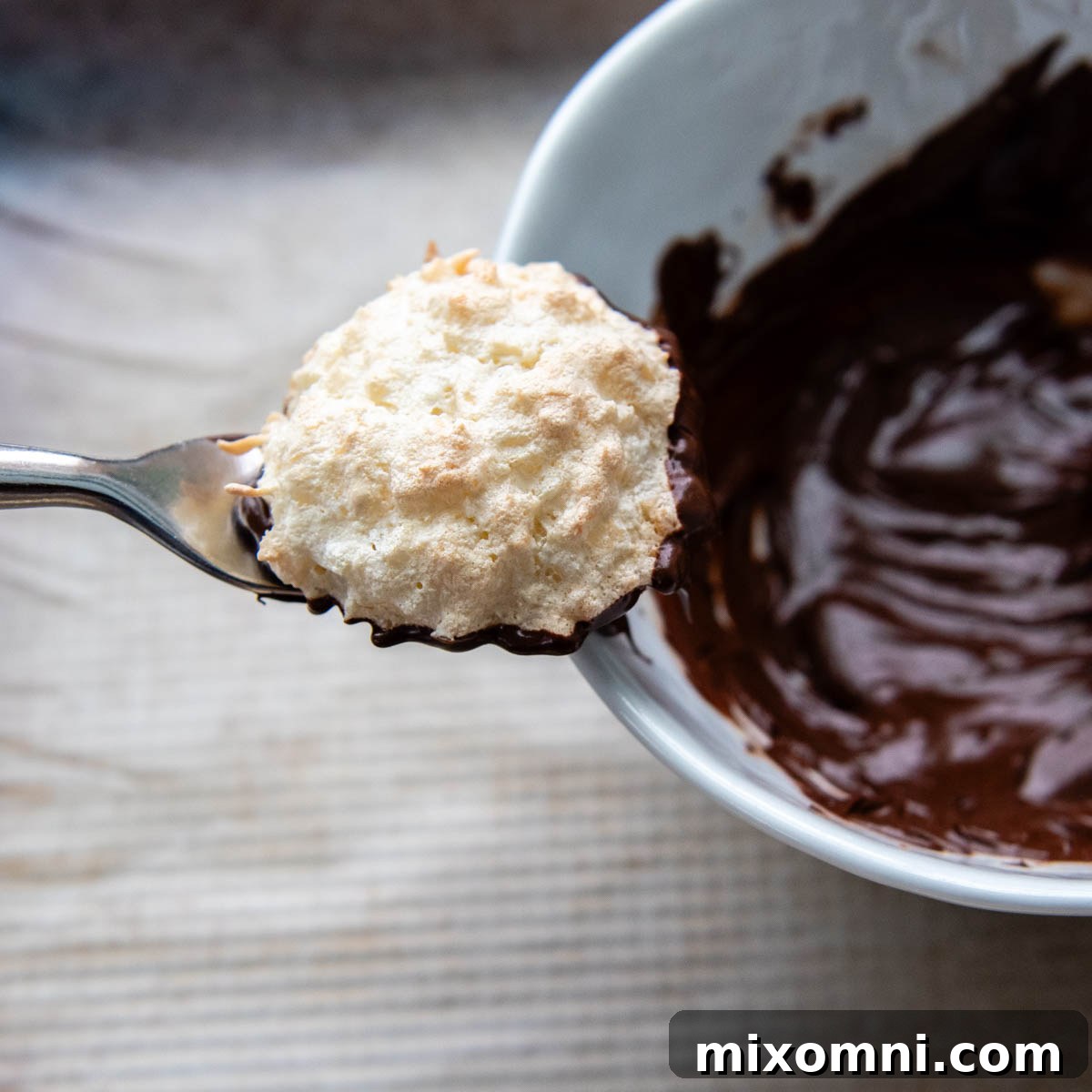 a macaroon coming out of a bowl of chocolate.