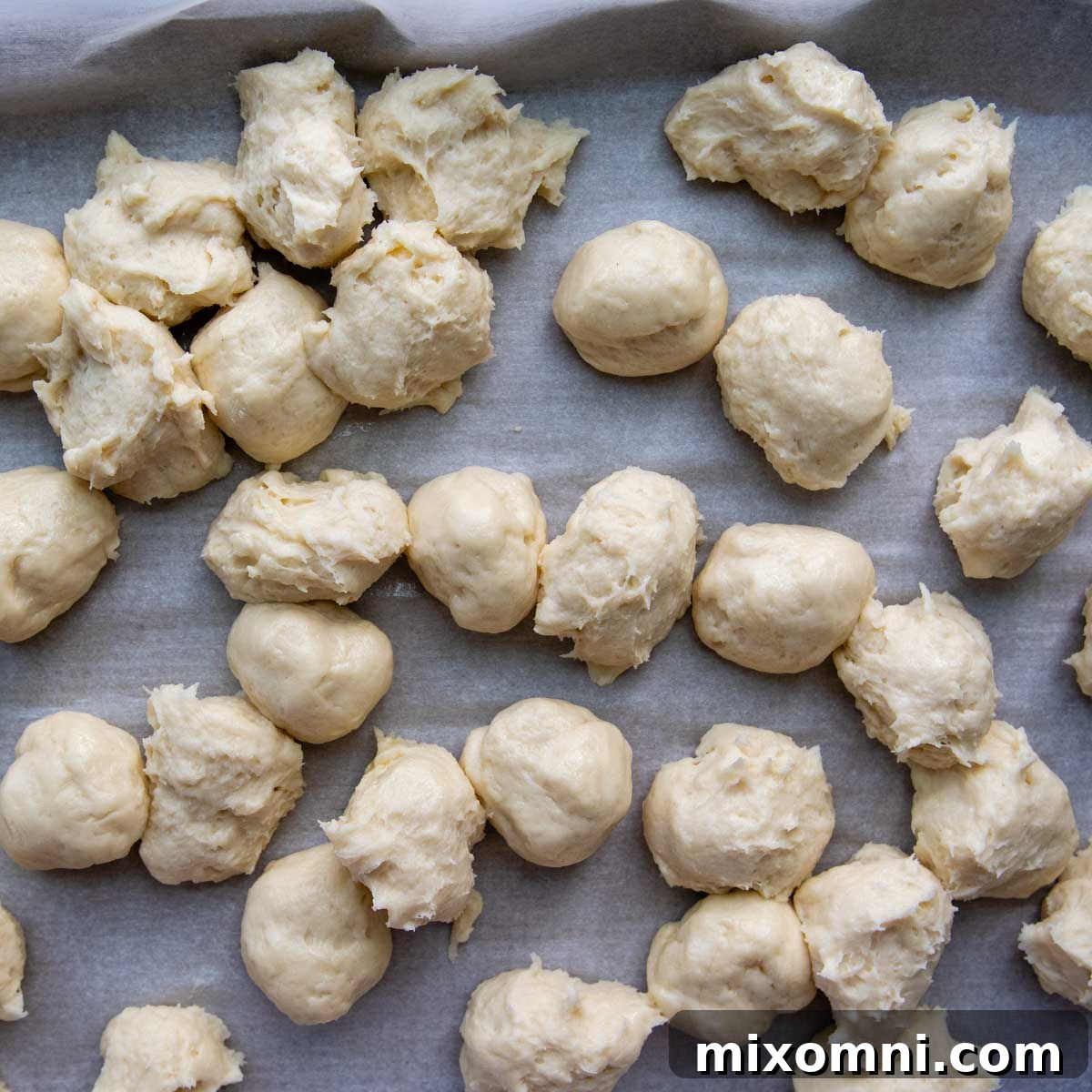 Portioned gluten-free dough balls scattered on a piece of parchment paper, ready for shaping.