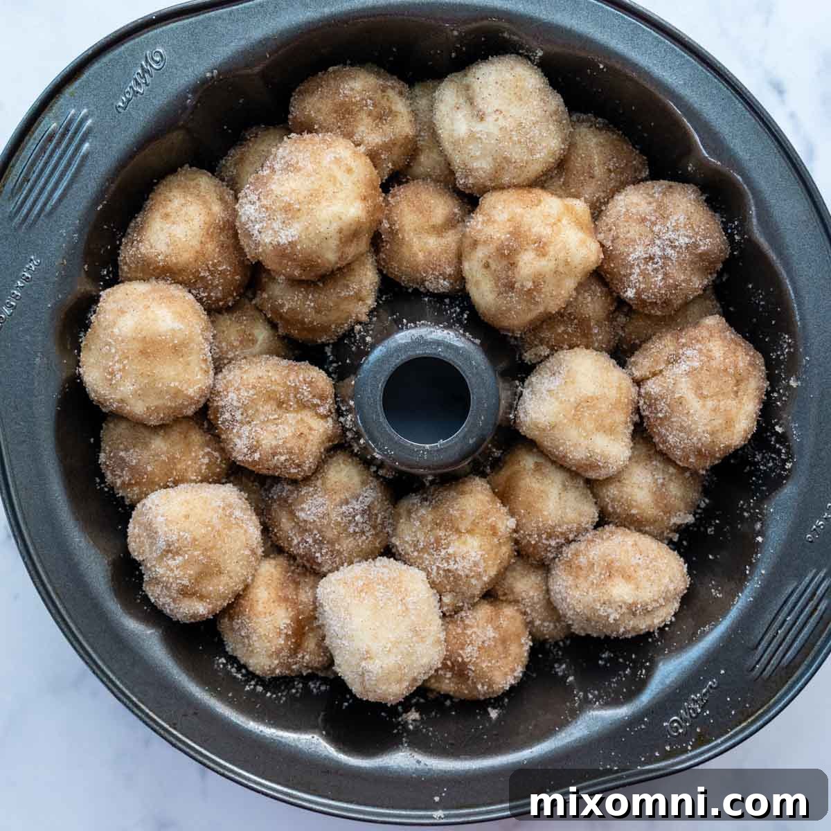 Unbaked cinnamon-coated dough balls meticulously layered in a bundt cake pan, ready for proofing.
