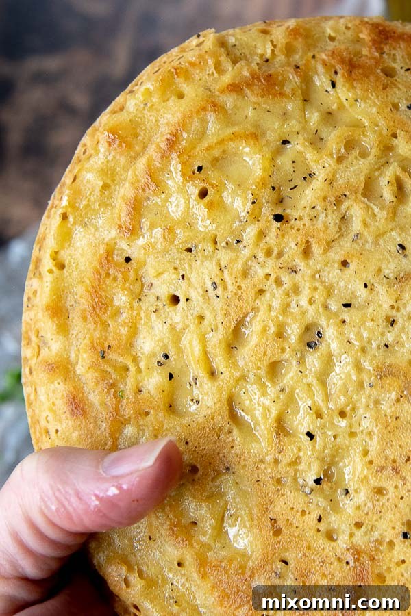 A close-up shot of a hand gently holding a golden-brown farinata flatbread, perfectly cooked with crispy edges, highlighting its inviting texture.