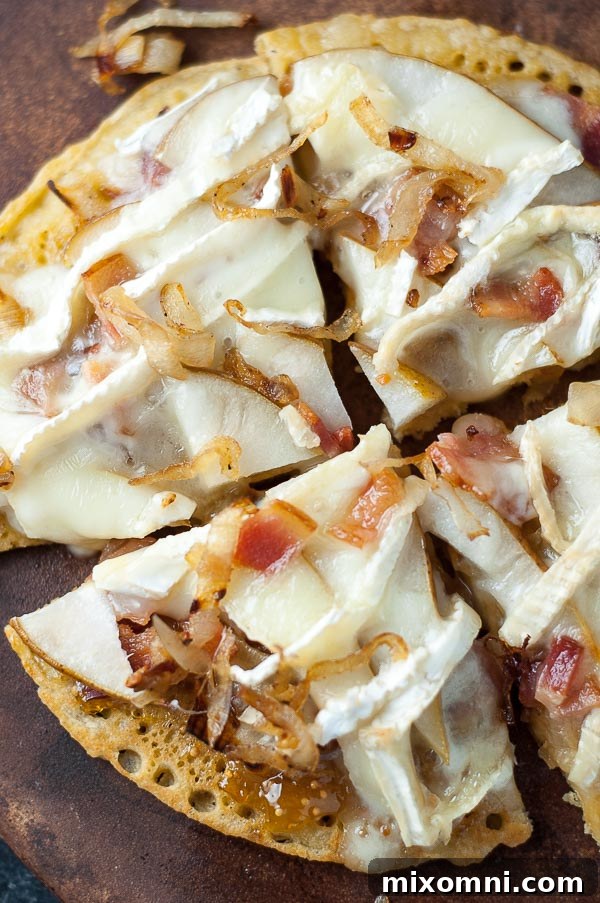 An overhead shot of a delicious and artfully prepared socca pizza adorned with thin pear slices, rich melted brie cheese, and crispy bacon, beautifully arranged and ready to be served.