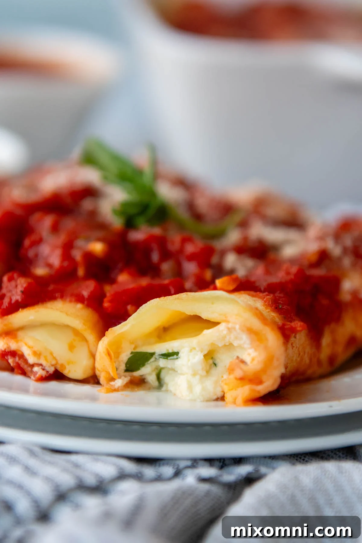 Close up of a delicious baked gluten-free manicotti on a white plate, showing the creamy ricotta filling and rich tomato sauce.