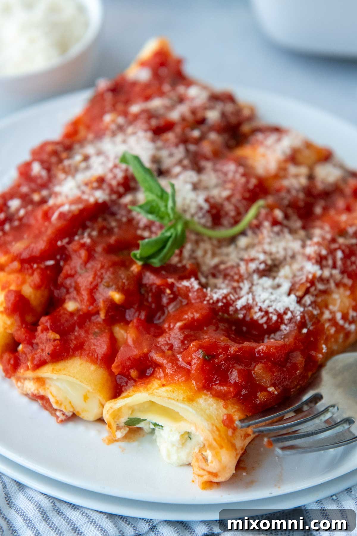 Three perfectly baked gluten-free manicotti shells on a plate, generously covered with tomato sauce and garnished with fresh basil leaves.