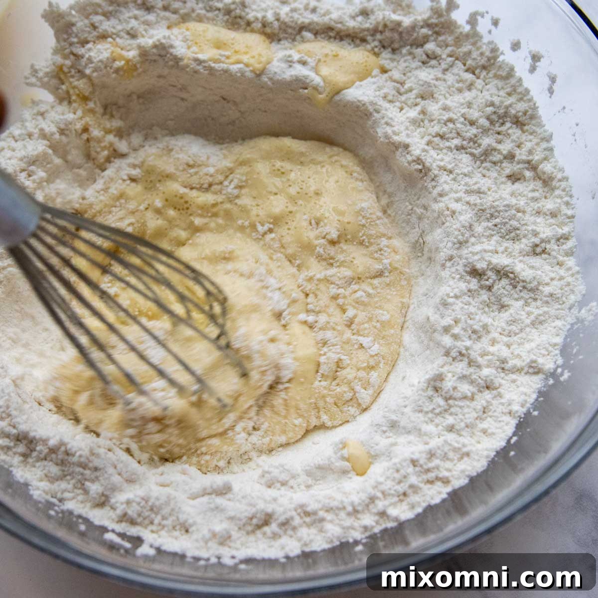 A person whisking gluten-free crepe batter in a large bowl, demonstrating the initial step for manicotti shells.