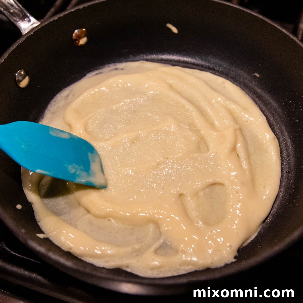 A thin layer of gluten-free crepe batter being spread evenly in a small nonstick skillet.