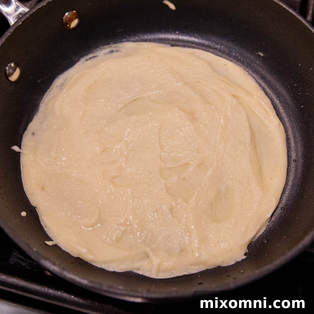 A gluten-free crepe showing opaque, mostly cooked surface, ready to be flipped in the pan.