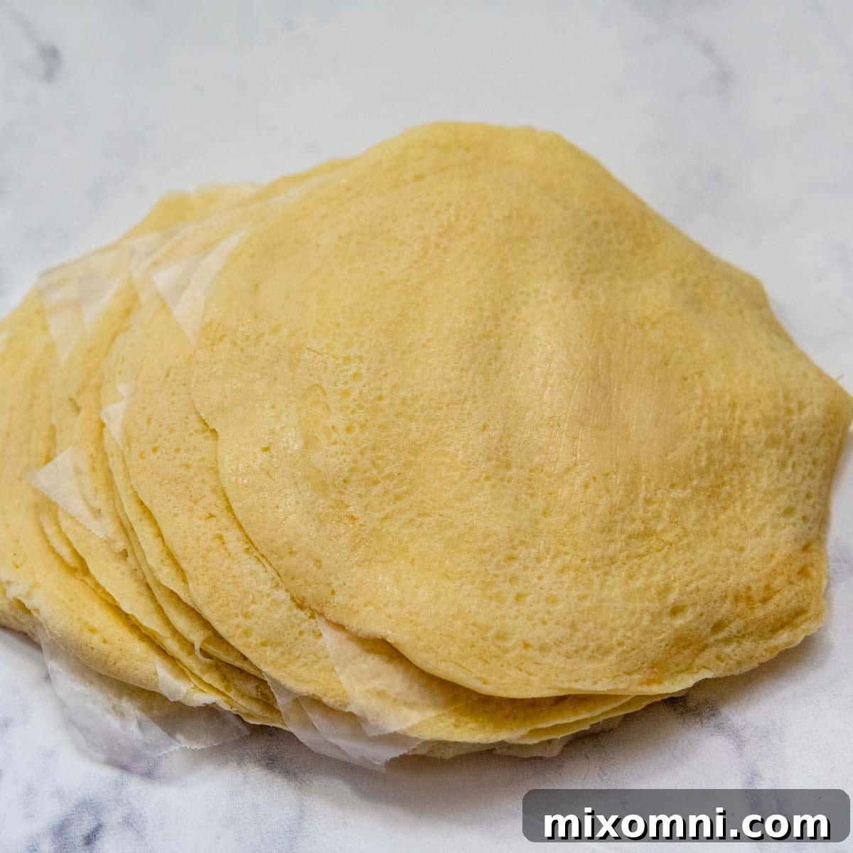 A neat stack of perfectly cooked gluten-free manicotti pasta shells, separated by wax paper.