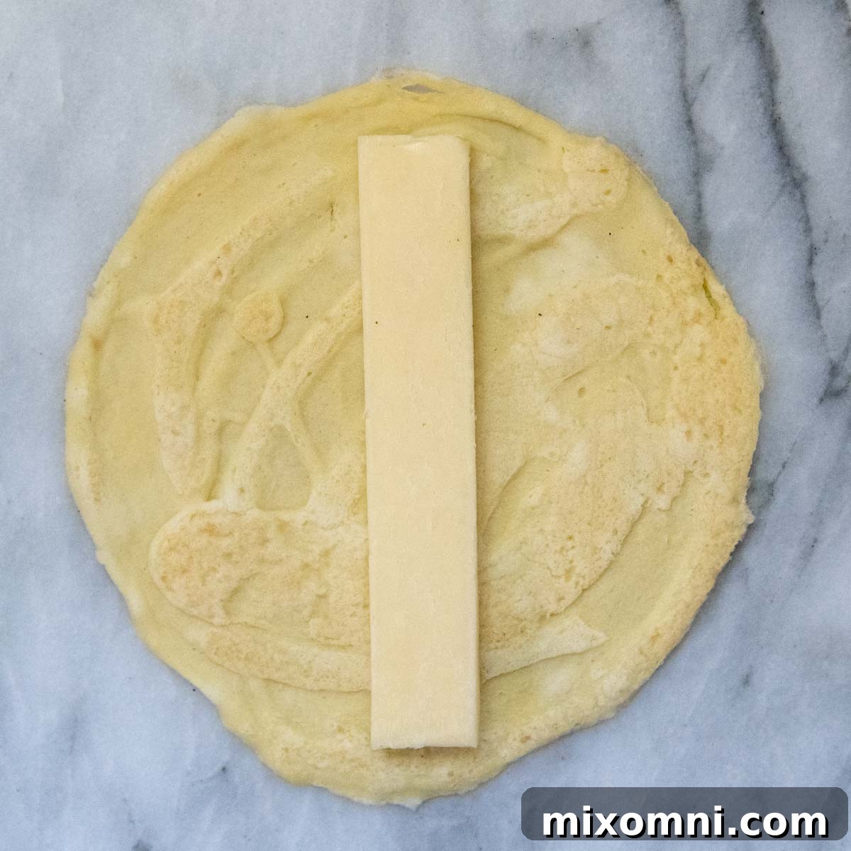 A slice of mozzarella cheese carefully placed on a homemade gluten-free crepe, ready for the ricotta filling.