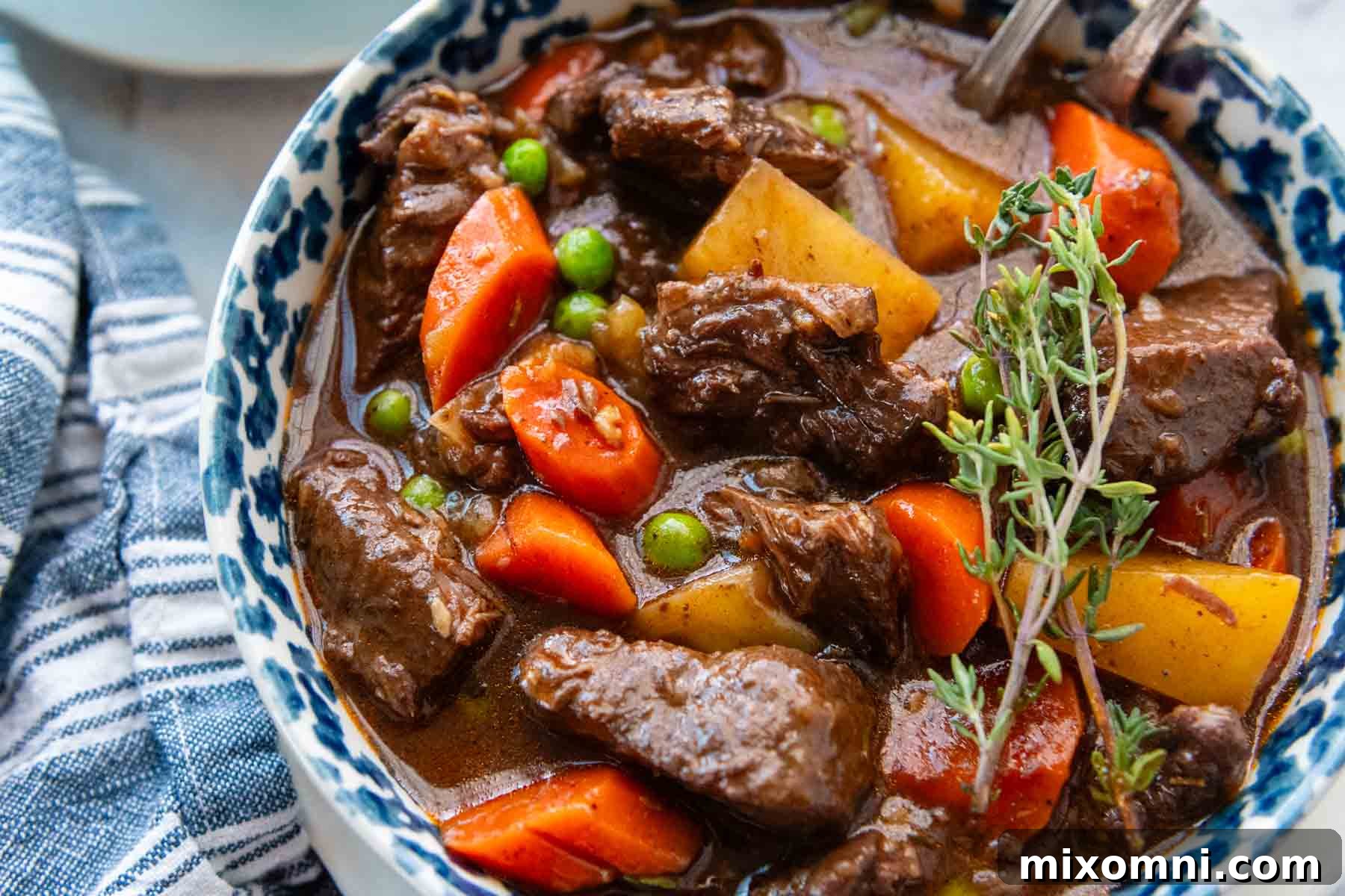 beef stew in a blue mottled bowl with fresh thyme.