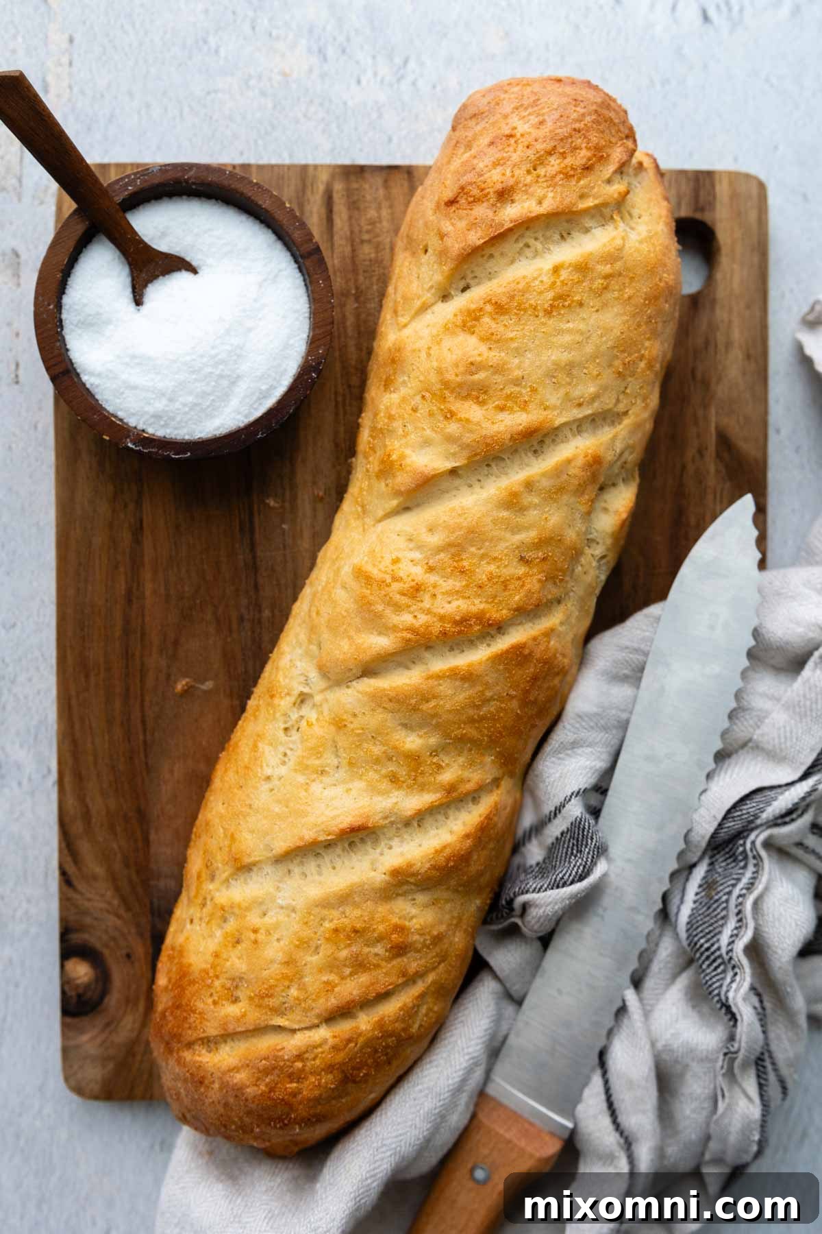 an entire loaf of Italian bread on a wooden cutting board with a small bowl of salt next to it.