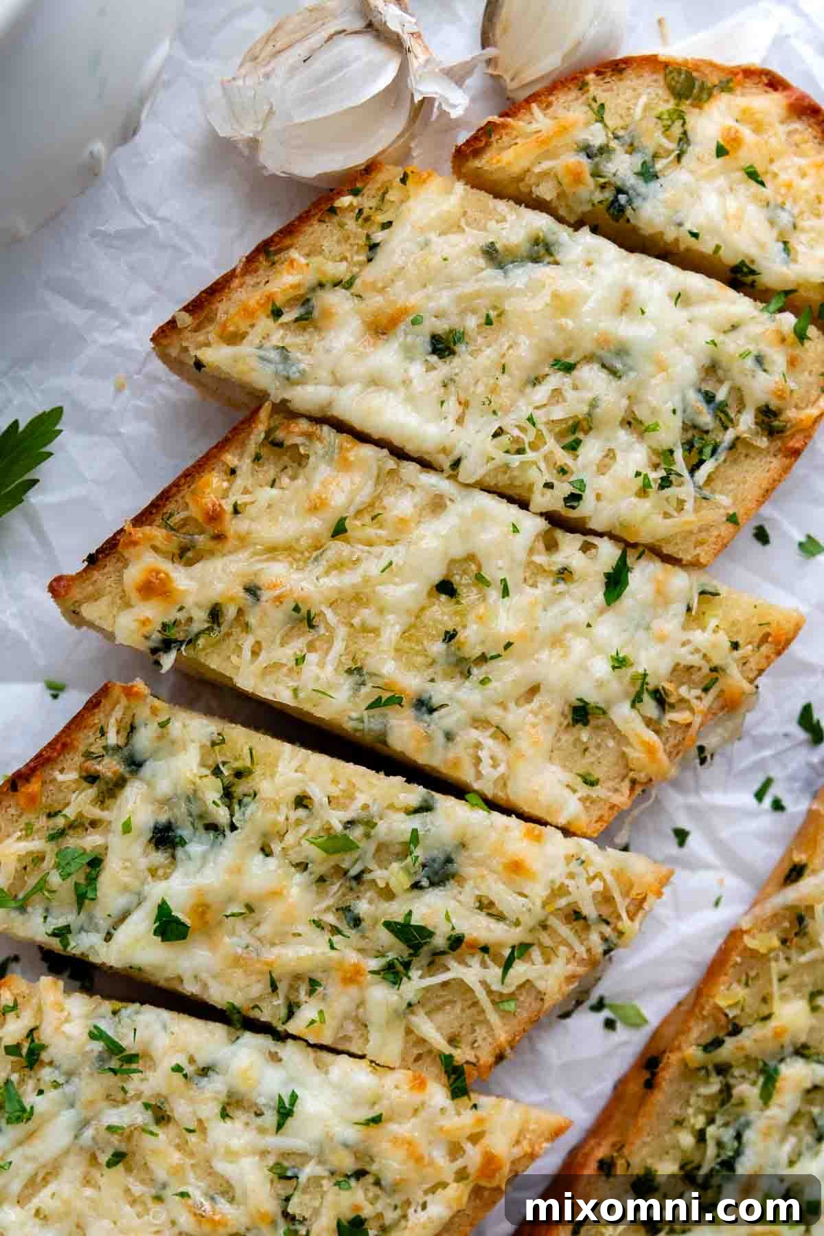 An overhead shot of freshly sliced gluten-free garlic bread, presented alongside whole garlic cloves, highlighting its readiness to serve.
