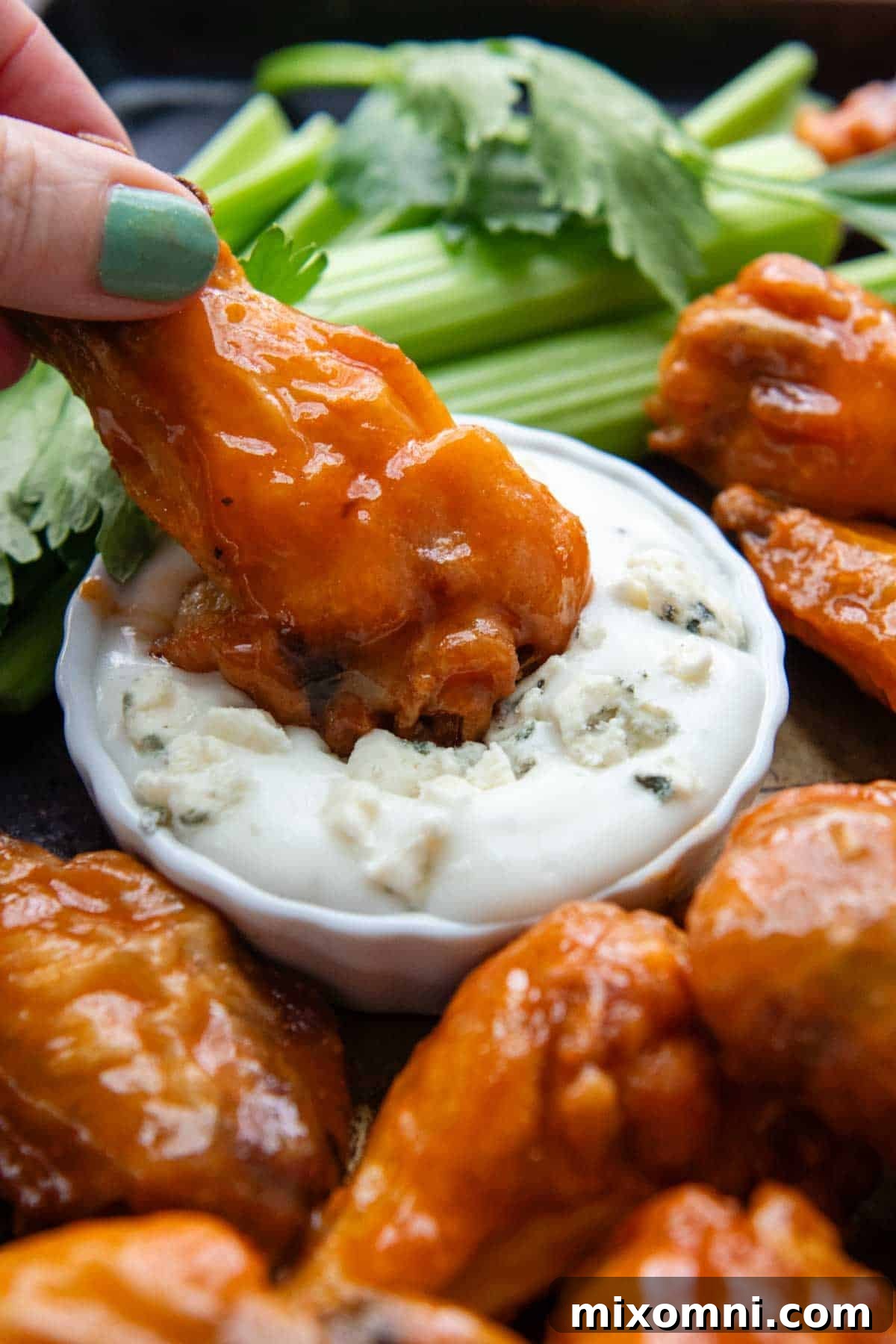 A buffalo drumette being dipped in blue cheese dressing, showcasing its crispy skin.