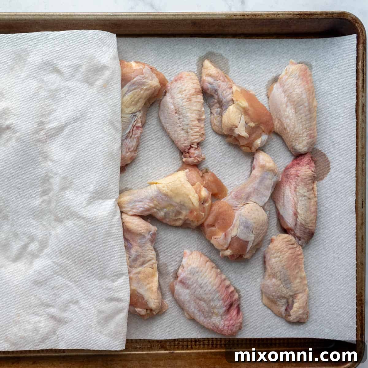 The wings being dried with paper towels on a baking sheet, ready for seasoning.