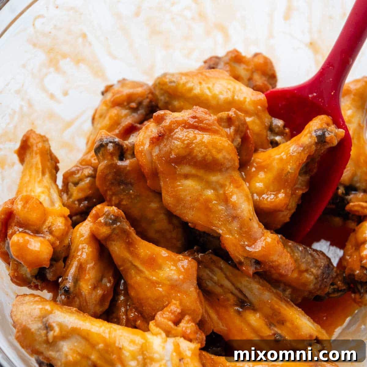 Baked wings being tossed in a bowl filled with buffalo sauce.
