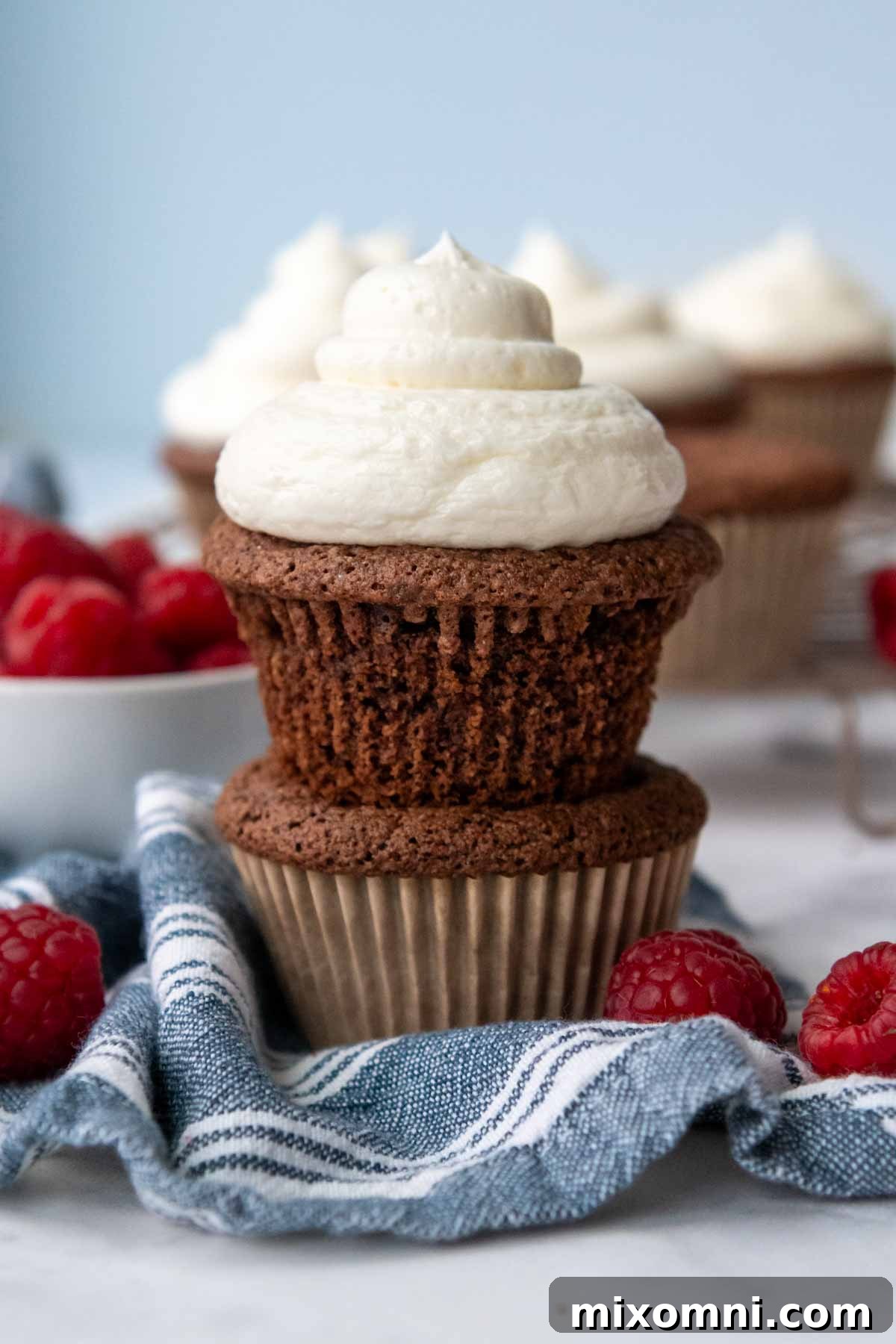 An unwrapped, frosted almond flour cupcake delicately placed on top of an unfrosted one.