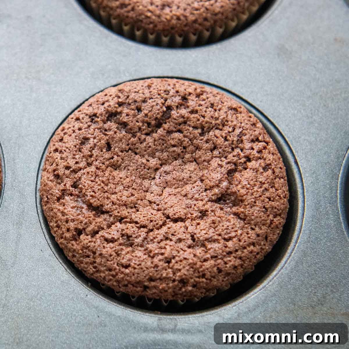 A perfectly baked almond flour cupcake sitting in a paper liner within a muffin tin.