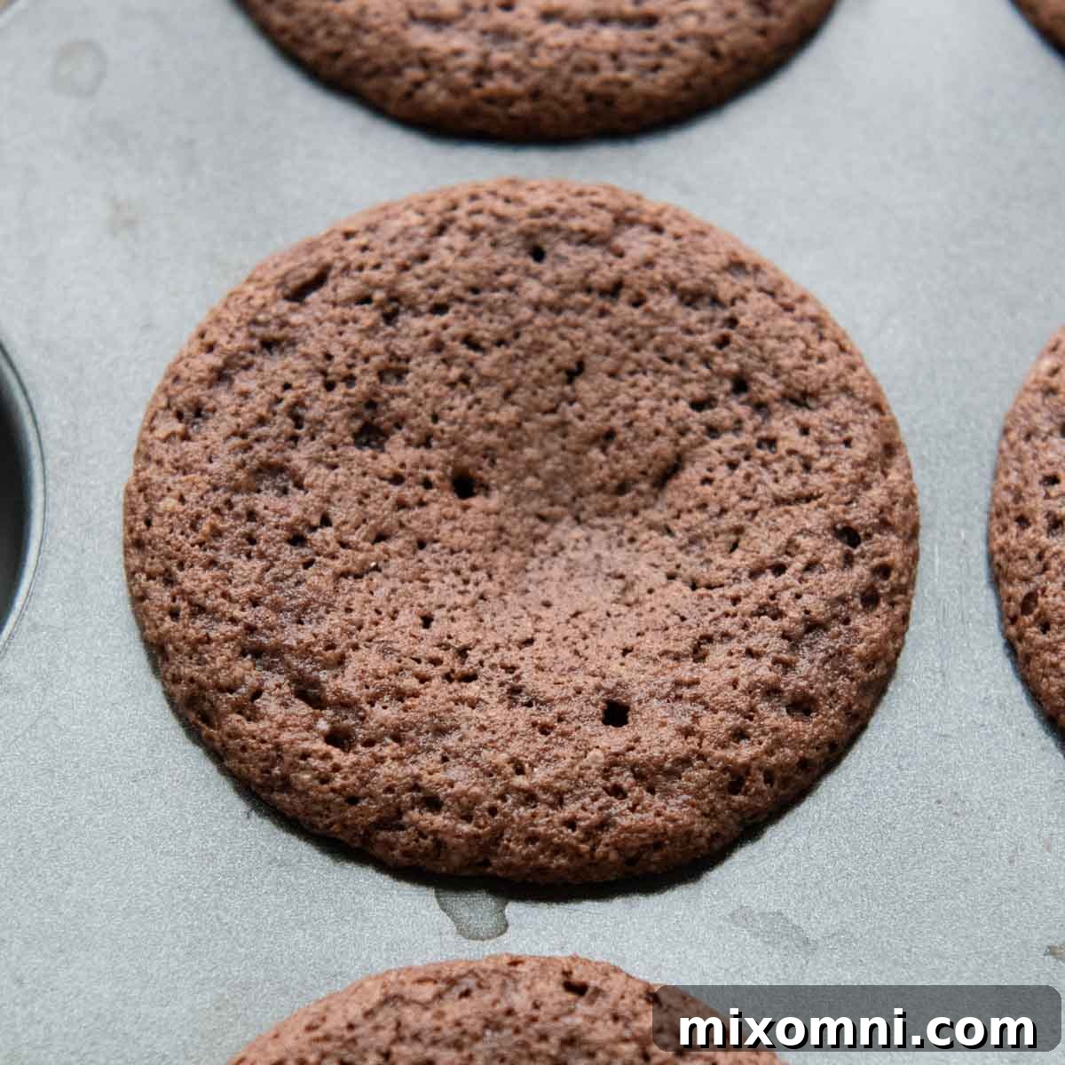 An overbaked and fallen almond flour cupcake in a muffin tin, illustrating baking problems.