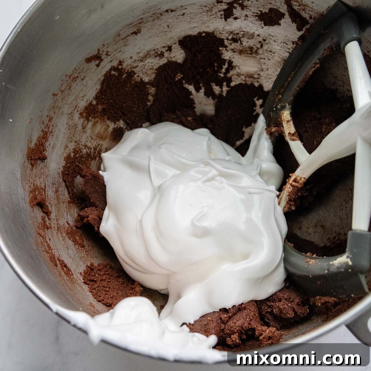 Stiffly beaten egg whites being gently folded into the thick chocolate almond flour batter.