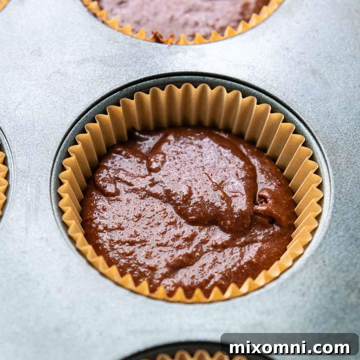 Unbaked chocolate almond flour cupcake batter meticulously portioned into paper-lined muffin tins.