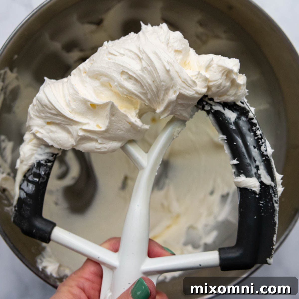 Fluffy almond buttercream frosting clinging to a mixer beater, showing its ideal consistency.