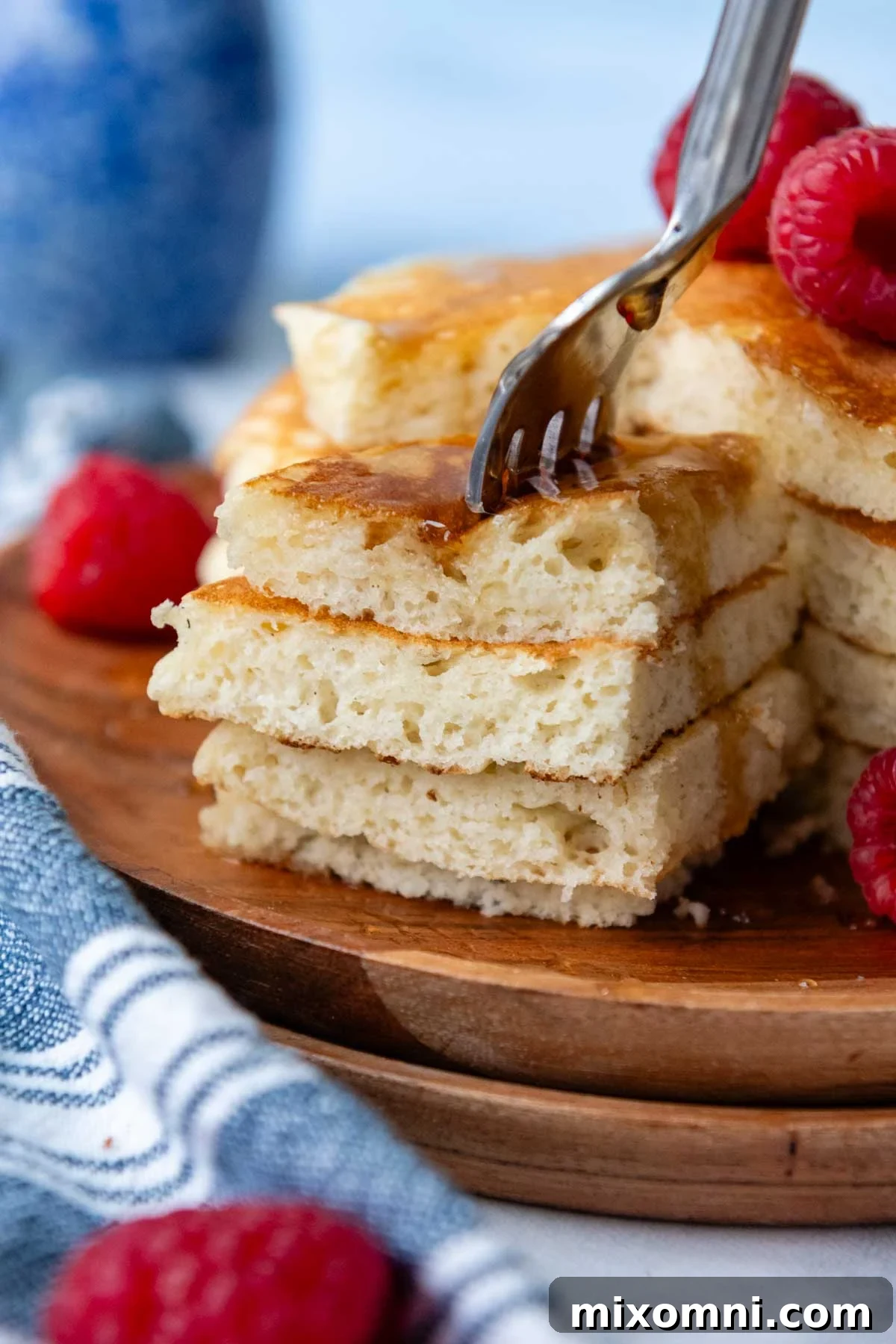 A fork piercing a stack of golden, fluffy gluten-free pancakes drizzled with syrup and topped with fresh berries.