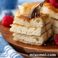 A fork piercing a stack of golden, fluffy gluten-free pancakes drizzled with syrup.