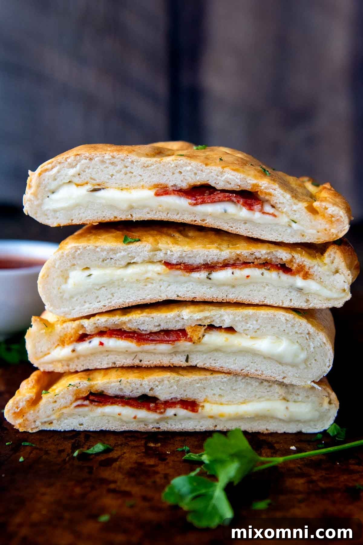 A tantalizing stack of golden-brown gluten-free calzones, each sliced in half to reveal their cheesy, flavorful interior, resting on a rustic wooden surface.