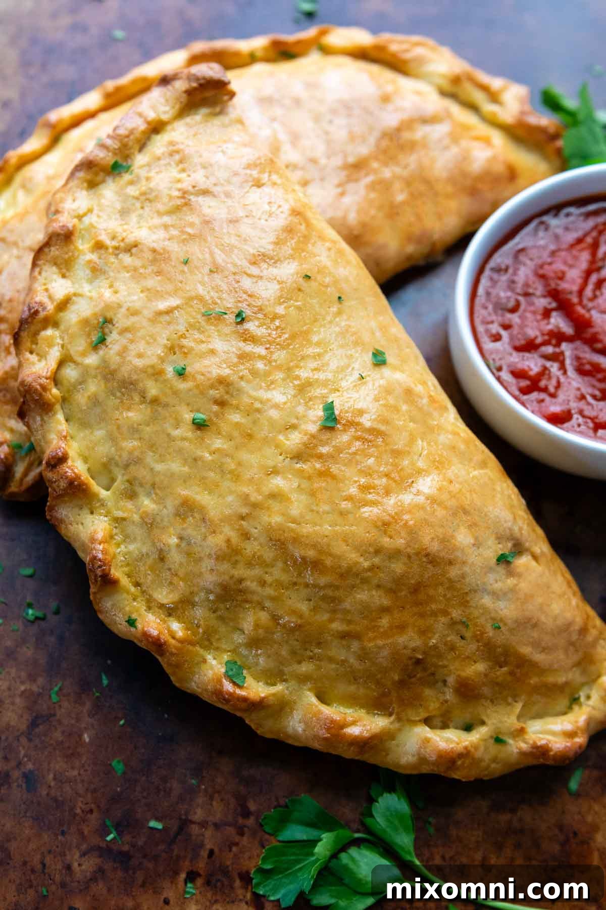A perfectly baked, golden-brown gluten-free calzone sitting next to a small dish of rich pizza sauce, ready for dipping.