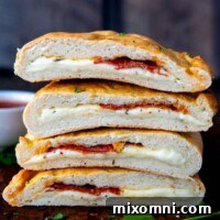 A stack of two gluten-free calzones, sliced in half, showcasing their rich, cheesy filling, on a cutting board.