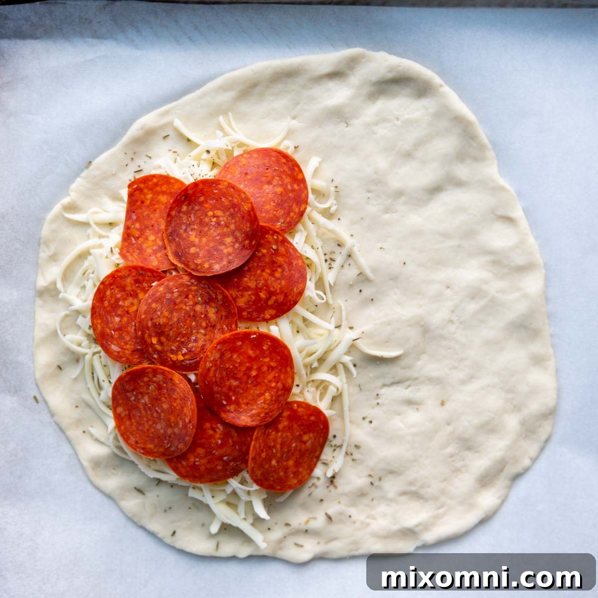 One half of a gluten-free calzone dough circle generously loaded with melted mozzarella cheese and various savory pizza toppings, leaving a clear edge for sealing.