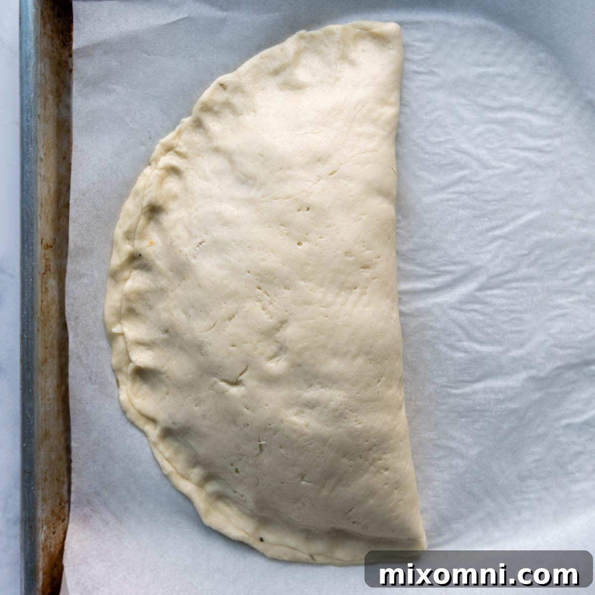 Close-up of calzone edges being firmly pressed together by hands to create a secure seal after folding the dough.