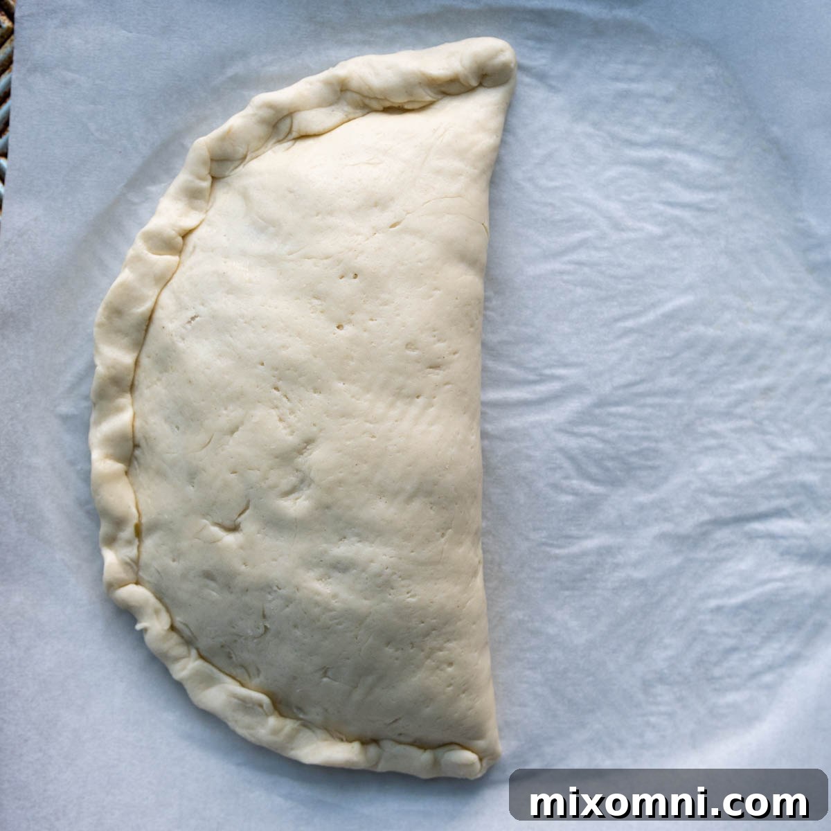 Hands demonstrating the technique of rolling the pressed calzone seam upwards towards the body of the calzone for an extra secure closure.