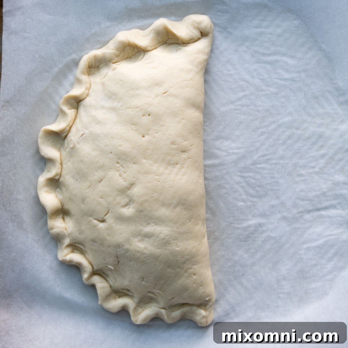 The final, beautifully crimped edge of a gluten-free calzone, resembling a classic pie crust, created with a thumb and forefinger.